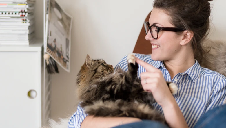 Žena se směje a hraje si s kočkou v náručí