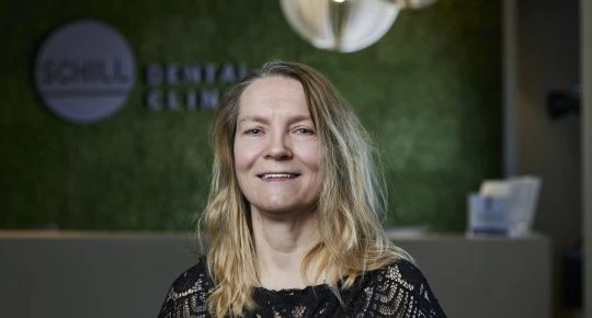 Žena usmívá se v recepci zubní kliniky s logem na zdi.