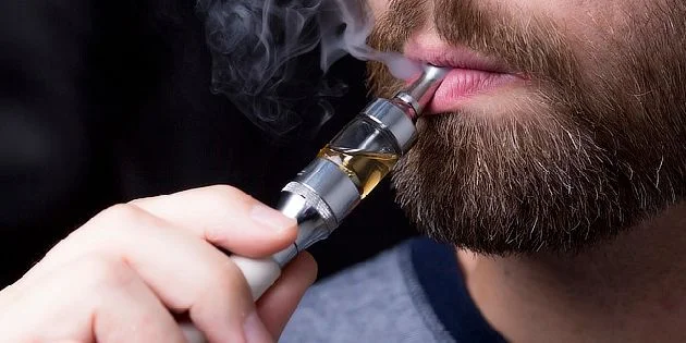 Muž s bradou kouří elektronickou cigaretu.
