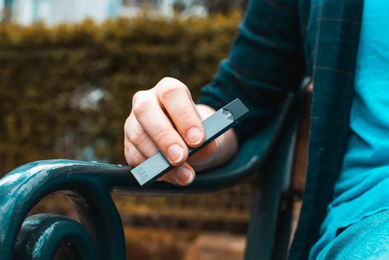 Ruka drží elektronickou cigaretu venku na lavičce.